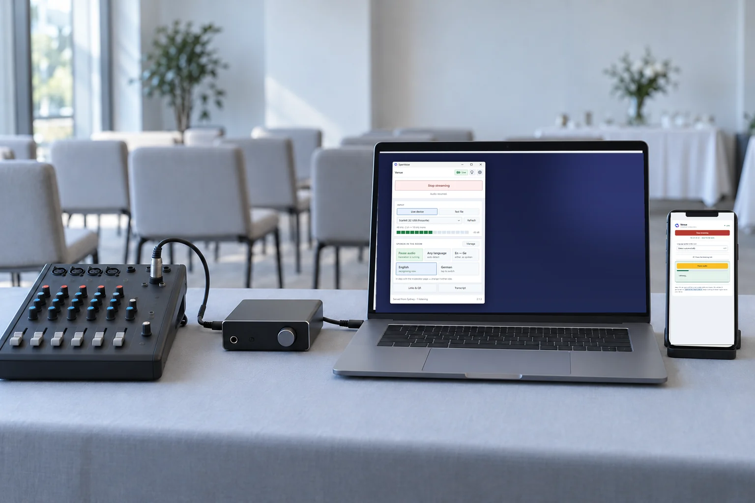 A small mixer feeding an audio interface and a laptop running the SpanVoice desk app, with a phone beside it showing the browser page.