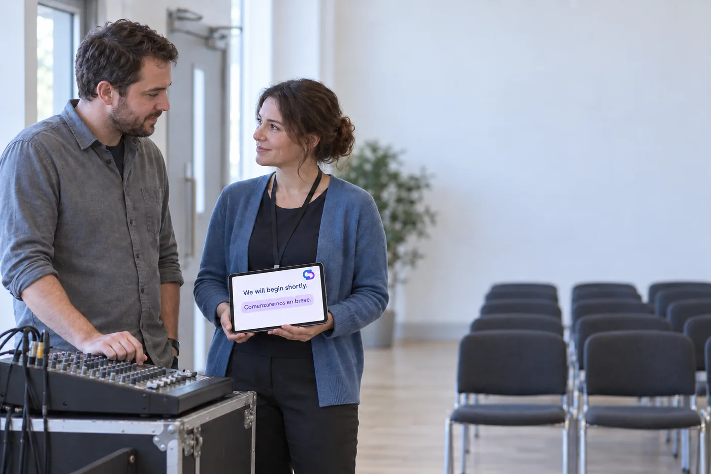 Two people preparing a hall before an event, cables run to a laptop at the sound desk.