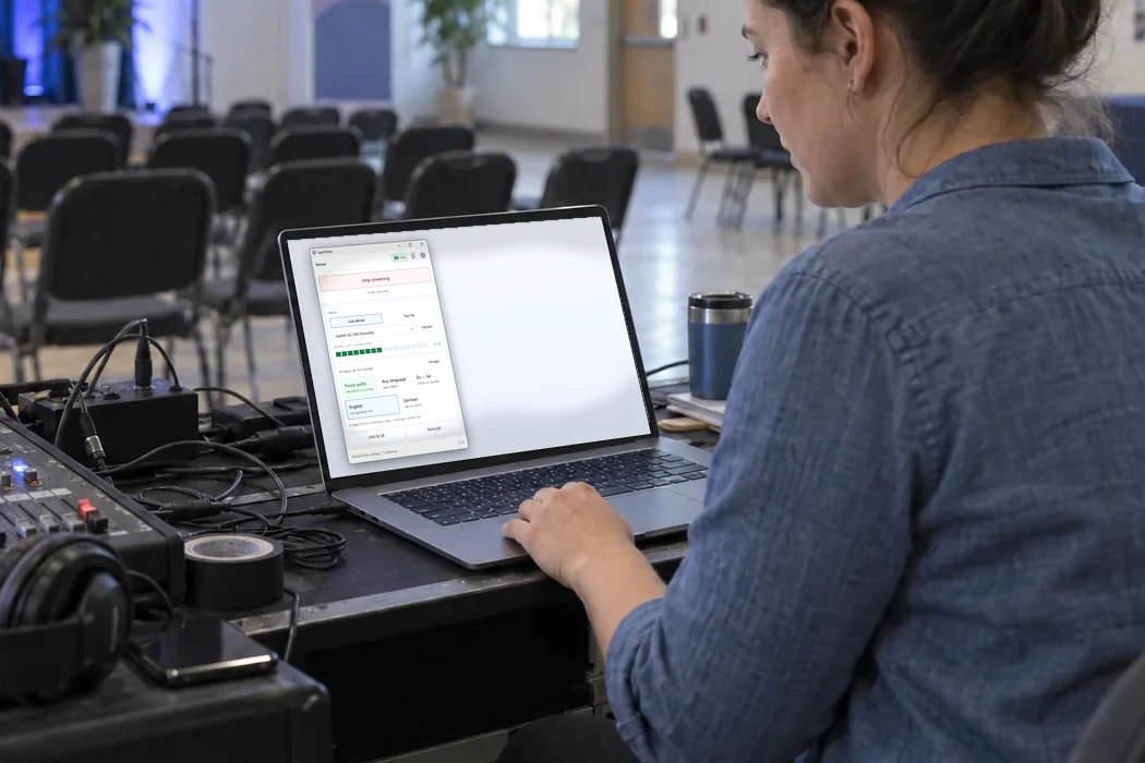 A volunteer at a sound desk at the back of a hall, the SpanVoice Windows app open on her laptop beside the mixer.